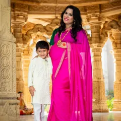 A beautiful family portrait taken at a temple. The mom-to-be, dressed in a stunning pink saree, stands with her son, blending tradition and family love.