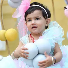 This is a lovely candid photo from a baby's first birthday shoot. Her curious expression as she holds the balloons tells a sweet story, showcasing her personality on her big day.