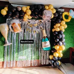 A fun 'Cheers to 18 Years' birthday party. This setup includes a black and gold balloon arch, a silver shimmer curtain, and large foil balloons shaped like a beer mug and champagne bottle.