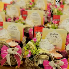 A collection of festive Diwali hampers in charming woven baskets. Each basket is filled with goodies, adorned with fresh flowers, and tied with a vibrant pink bow, ready to spread joy and light during the festive season.