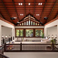 The mezzanine lounge of the Dream Coffee Estate, a sanctuary held within a soaring terracotta roof. Light pours in from glass skylights and large windows, illuminating the warmth of the wood and creating a space for quiet contemplation, high above the forest floor.