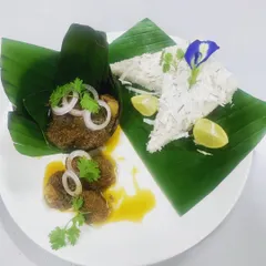 A beautifully plated breakfast of Pandi Curry and Paputtu, a traditional Coorgi steamed rice cake. Garnished with fresh onion, coriander, and a squeeze of lime, it’s a true taste of home.