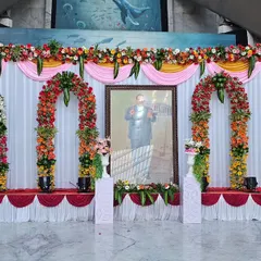 This is a complete stage setup I created for a formal tribute event at ONGC. The design includes a clean white backdrop with draped fabric, multiple floral arches, and professional stage lighting to create a respectful and distinguished ambiance.