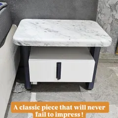 This classic nightstand will never go out of style. It features a white marble top, a sturdy dark frame, and a contrasting white drawer with a sleek black handle.