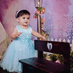 A baby girl in a lovely blue dress stands by a miniature park bench and lamppost. This themed setup shows the creative and detailed environments I build for baby photoshoots.