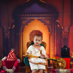 A full view of our 'Shivaji Maharaj' setup, where a young boy sits on a throne, holding a toy sword, surrounded by a shield and other warrior props against a royal backdrop.