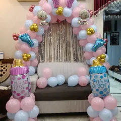A classic "It's a Boy, It's a Girl" themed baby shower or gender reveal decoration. The balloon arch is decorated with baby bottle foil balloons and a silver shimmer curtain.