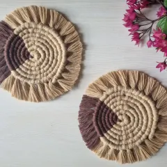 A pair of spiral macrame coasters, styled with a small flower to show how they can brighten up any tabletop.