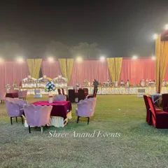 A wide shot of an outdoor wedding venue at night. The image captures the spacious lawn with elegant guest seating and the long, beautifully lit buffet line in the background, showcasing the scale of the event.