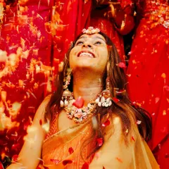 A moment of pure bliss. The bride looks up with a wide smile as she is showered with red flower petals during her Haldi ceremony.