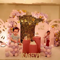 A magical butterfly-themed first birthday for a little princess. This elegant setup features large butterfly wing cutouts, a soft pastel color palette of pink and lavender, and a sparkling gold backdrop.