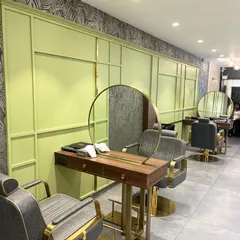 A styling station at the Madonna Salon, featuring a vibrant lime green paneled wall and a custom circular mirror with brass accents. The design combines bold color with elegant materials to create a fresh and modern look.