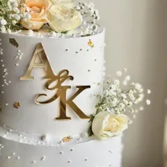A close-up on the details that matter. This shot highlights the crisp gold monogram, delicate gold leaf, and tiny edible pearls that give this engagement cake its luxurious feel.