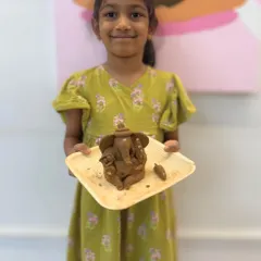 The proud smile of a young artist holding her finished clay Ganesha. Our workshops are designed to build confidence and let little hands create big, beautiful things.