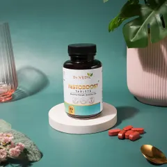 A bright and fresh e-commerce shot for Dr. Vedic Testoboost tablets. The use of a pink pot and a green plant adds a touch of lifestyle context while keeping the focus on the product.