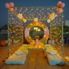 A romantic rooftop cabana setup, perfect for a "Bride to Be" party or an intimate celebration. The design includes a frame draped with fairy lights, a circular balloon arrangement, and low seating for a cozy and magical evening.