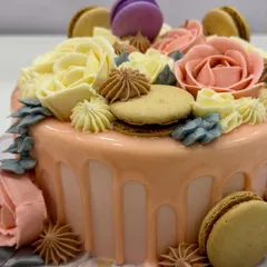A close-up of one of the three cakes from the celebration: a vanilla sponge with white chocolate ganache, buttercream roses, a white chocolate drip, and macarons.