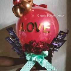 A custom balloon bouquet featuring a large red balloon, fresh flowers, and an assortment of chocolates, perfect as a gift or centerpiece.