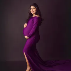 We love a bold color choice. This stunning off-the-shoulder purple gown creates such a striking and powerful silhouette, beautifully highlighting the baby bump against a classic dark backdrop.