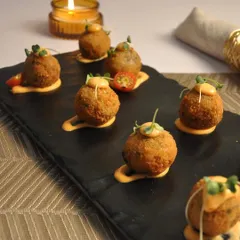 These are my crispy Arancini Balls, served on a slate platter with a drizzle of sauce and microgreens. They are a perfect bite-sized appetizer for festive occasions like Diwali, offering a gourmet touch to your party menu.