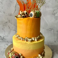 A two-tier version of my Lohri celebration cake, featuring a vibrant orange and yellow ombre design, edible bonfires, and dhol accents.