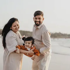 A playful moment on the beach as parents swing their laughing one-year-old. The ocean waves and open sky create a feeling of freedom and joy.