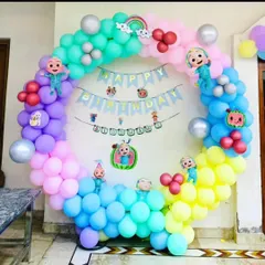 A colorful Cocomelon themed birthday decoration with a circular balloon arch, character cutouts, and a "Happy Birthday" banner.