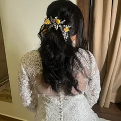 A romantic half-up hairstyle for a Christian bride. Soft curls are gathered at the back and adorned with delicate yellow flowers and pearls, perfectly matching her white lace gown.