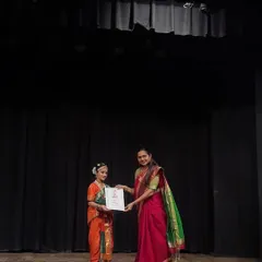 Presenting a certificate to a young student in her vibrant orange and green costume. These moments on stage are what we work towards in our classes, building confidence and performance skills.