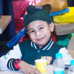 A charming portrait of a young boy in a turban, smiling gently at the camera during a party.