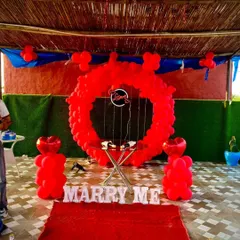 This is a popular proposal decoration package. It features a full circle balloon arch in vibrant red, "MARRY ME" marquee letters, and a small table for a cake or champagne, perfect for a terrace or garden proposal.