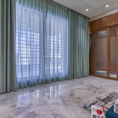A spacious bedroom featuring a large wardrobe with frosted glass and wood sliding doors. The sheer curtains allow for soft, diffused natural light, creating a calm and airy atmosphere.