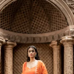 A regal peach-orange silk half saree, embodying a blend of traditional elegance and modern charm. The embroidered organza dupatta adds a layer of sheer beauty.