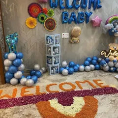 A complete "Welcome Baby" decoration for a baby boy, including blue and silver balloons, "BABY" display boxes, foil balloons, and a traditional flower petal "WELCOME" message on the floor.