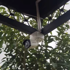 A Hikvision IP camera neatly installed under a metal awning. I ensure the placement protects the camera while providing an optimal viewing angle.