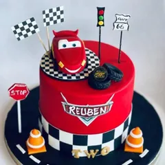A "Cars" movie themed cake for a little fan named Reuben. This cake features Lightning McQueen on a racetrack, complete with traffic lights, cones, and checkered flags for a fun birthday.