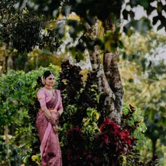 A graceful portrait of a bride in a pink saree, standing amidst lush greenery, showcasing her calm and elegant presence.