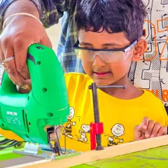 Safety goggles on! This student is fully focused while learning to operate a jigsaw with an instructor's help. This is a core part of our hands-on skill development program.