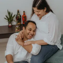 An authentic moment of laughter and affection during an at-home maternity shoot. The husband rests his head on her lap, showcasing the comfort and intimacy that can be captured in a familiar environment.