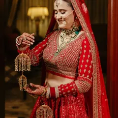 A radiant bride in her red lehenga, smiling as she holds her 'kalire', captured in a moment of happy anticipation.