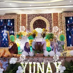 A luxurious and grand jungle safari stage for Yunay's first birthday. The opulent backdrop is covered in flowers, with large, realistic 3D animal props like a lion, giraffe, and tiger creating a truly immersive and high-end safari experience.
