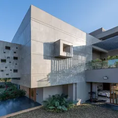 Here you can see the interplay of different volumes and textures. The solid, raw concrete structure is contrasted with a glass-railed balcony and recessed windows, creating a facade that is both powerful and intricately detailed.