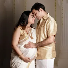 Celebrating heritage and love. This couple's portrait, featuring a traditional white and gold Kerala saree, beautifully blends cultural elegance with the intimacy of the maternity journey in a classic studio setting.