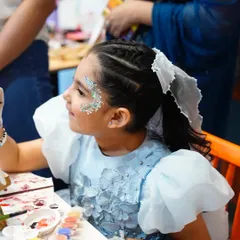 A young guest with beautiful glitter face paint gets creative at the art station during a 'Frozen' party.