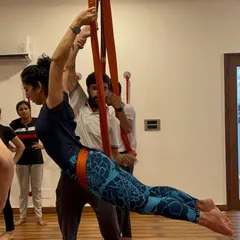 Learning to teach Aerial Yoga requires hands-on practice. Here, an instructor guides a trainee through a supported pose.