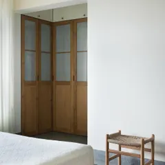 A minimalist stool with a handwoven seat, placed at the foot of the bed. I design small, versatile pieces like this to add texture and utility, providing a simple spot to rest or place things.