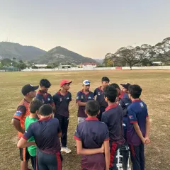 A team huddle during our international tour in Trinidad. Our coach strategizes with the team against a scenic mountain backdrop.
