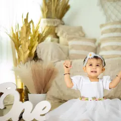 A little princess celebrating her first birthday. The simple white dress and clean, bright background create a timeless and elegant portrait.