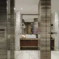 The master bathroom in the Caitriona apartment is a study in architectural elegance. Arbascato and Ebony travertine marble clad the walls and floors, while the custom vanity features an Aukupira veneer front and a brass base, creating a rich and luxurious palette.