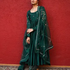 I love making colors speak. Here, the deep emerald green of the Anarkali suit is the hero, set against a rich red backdrop. This is a perfect example of a lookbook shot that highlights the garment's regal quality and intricate embroidery.